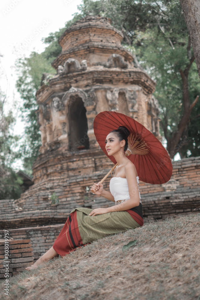 Beautiful Thai women wearing traditional Thai clothes holding ancient red umbrellas in temples Thailand, woman concept