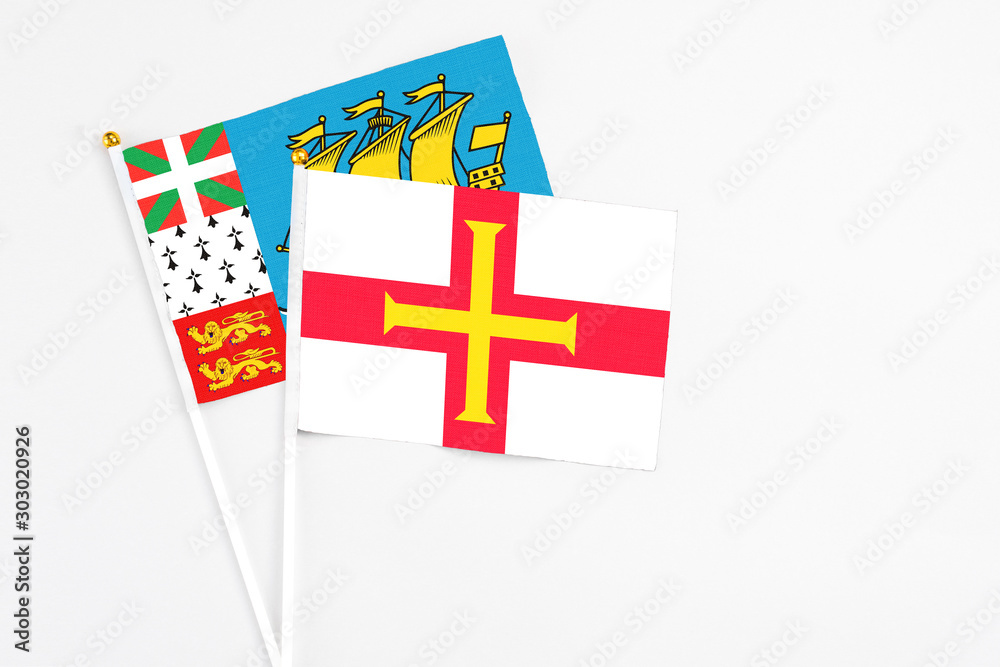 Guernsey and Saint Pierre And Miquelon stick flags on white background. High quality fabric, miniature national flag. Peaceful global concept.White floor for copy space.
