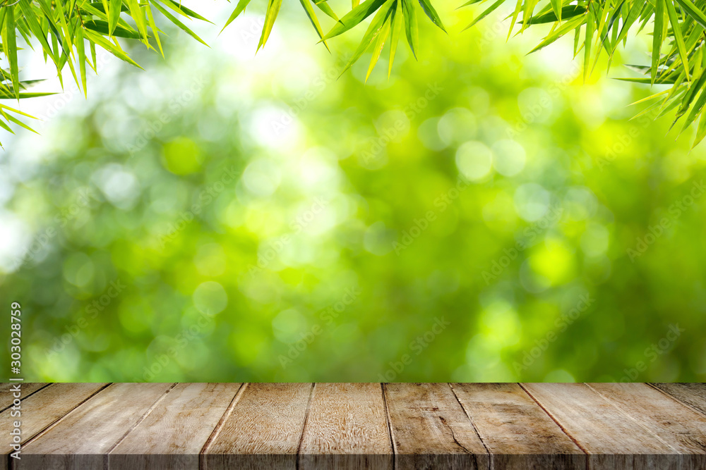 Empty old wooden table top with bamboo leaves frame on blurred greenery background in garden. Copy space for your display or montage product design. Empty old wooden table top with bamboo leaves frame on blurred greenery background in garden. Copy space for your display or montage product design.