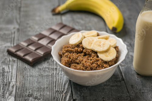 Chocolate, banana and a bowl of quinoa porridge on a black wooden table.
