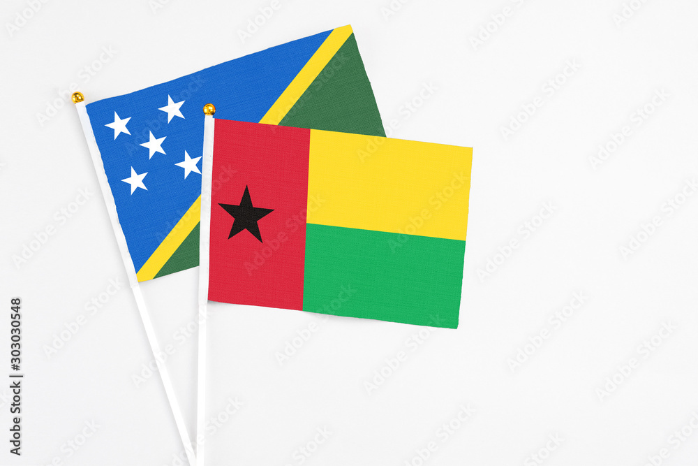 Guinea Bissau and Solomon Islands stick flags on white background. High quality fabric, miniature national flag. Peaceful global concept.White floor for copy space.