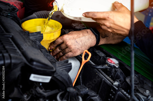Car maintenance concept.Car mechanic replacing and pouring fresh oil into engine at maintenance service station.Auto repair technician pour new engine oil to replace the old one