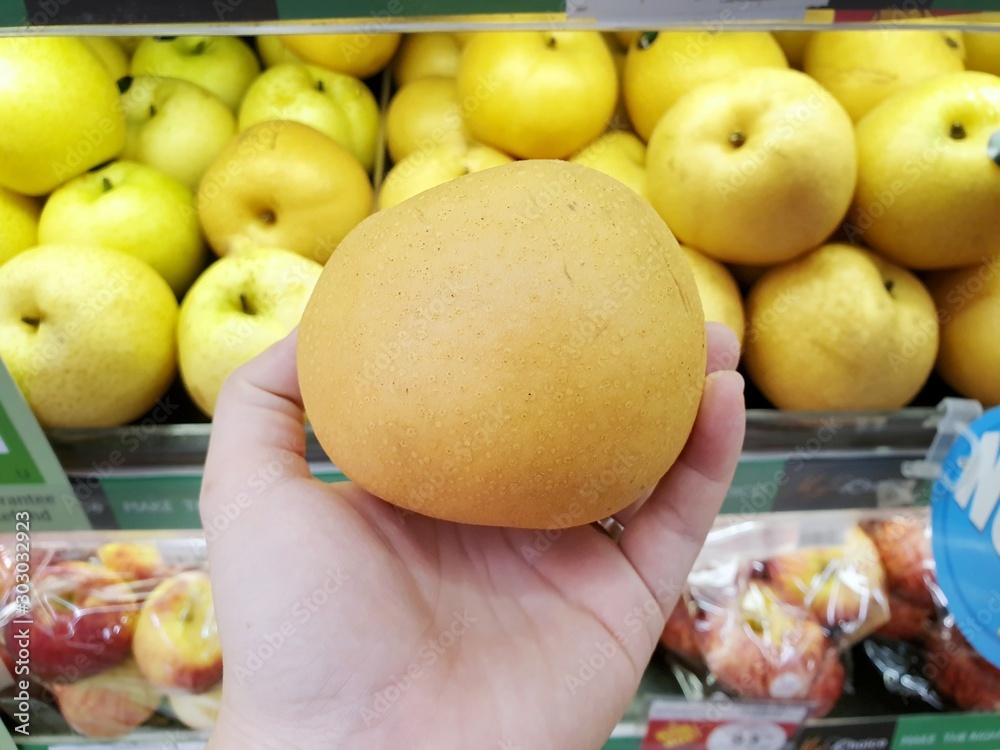 Φωτογραφία Selective focus of hand holding Chinese pear for sale on market stand in superma