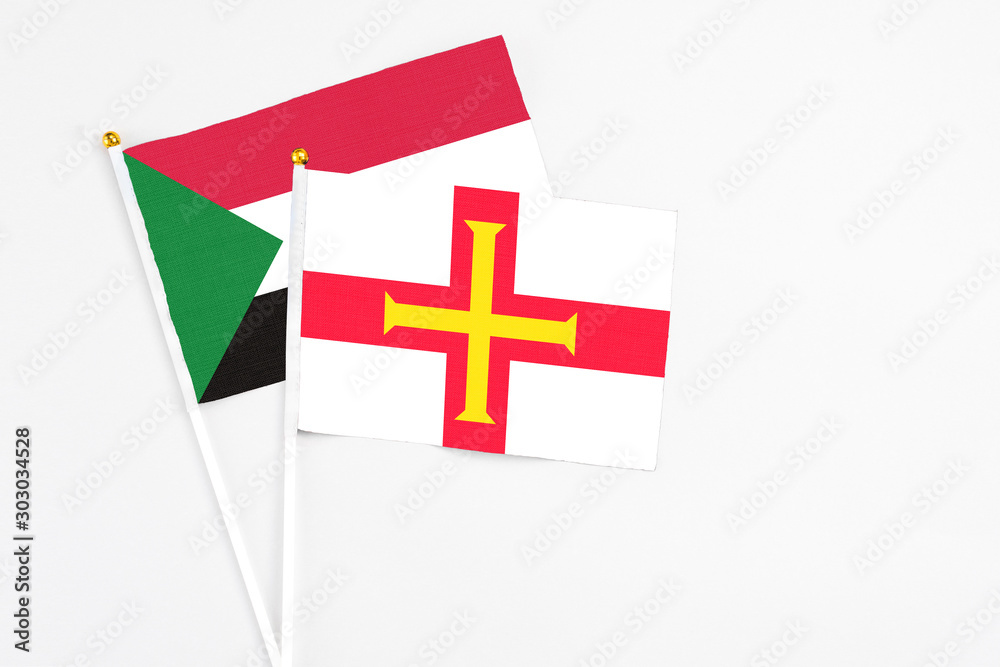 Guernsey and Sudan stick flags on white background. High quality fabric, miniature national flag. Peaceful global concept.White floor for copy space.