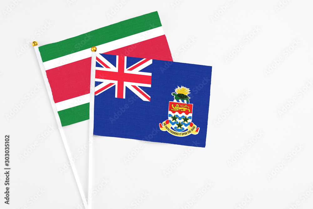 Fototapeta premium Cayman Islands and Suriname stick flags on white background. High quality fabric, miniature national flag. Peaceful global concept.White floor for copy space.