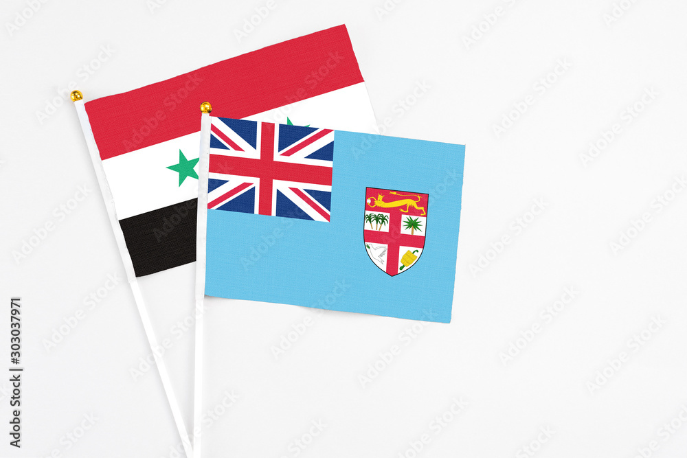 Fototapeta premium Fiji and Syria stick flags on white background. High quality fabric, miniature national flag. Peaceful global concept.White floor for copy space.