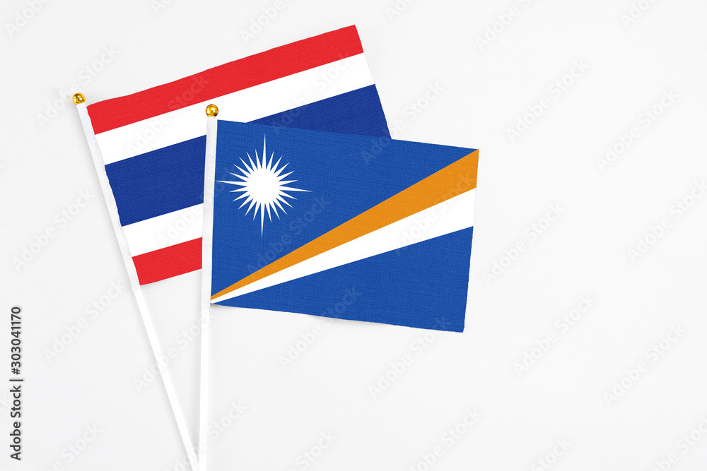 Fototapeta premium Marshall Islands and Thailand stick flags on white background. High quality fabric, miniature national flag. Peaceful global concept.White floor for copy space.