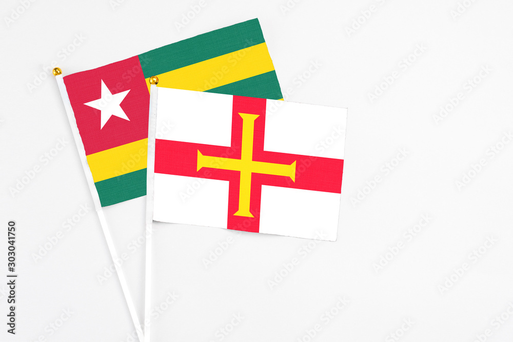 Guernsey and Togo stick flags on white background. High quality fabric, miniature national flag. Peaceful global concept.White floor for copy space.