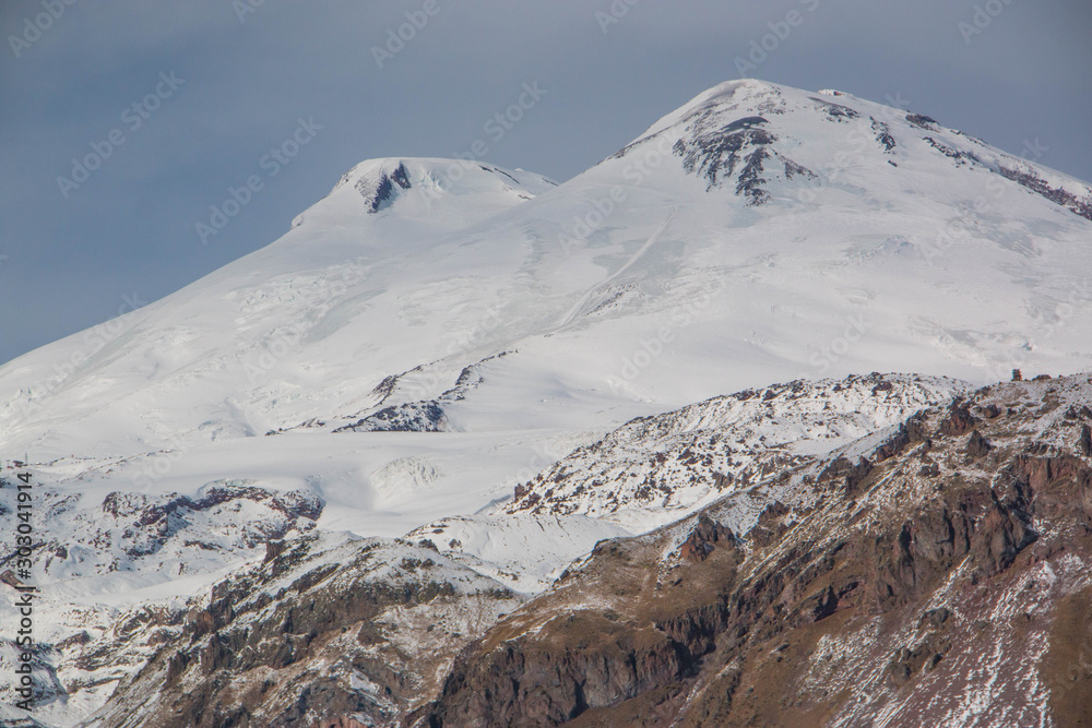 Snowboarder going down the slope of mount Elbrus. He wore bright clothes: yellow pants and a turquoise jacket, with a helmet on his head. The picture was taken in November.