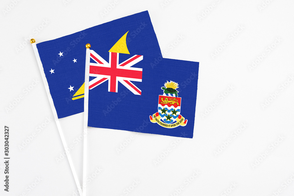 Fototapeta premium Cayman Islands and Tokelau stick flags on white background. High quality fabric, miniature national flag. Peaceful global concept.White floor for copy space.