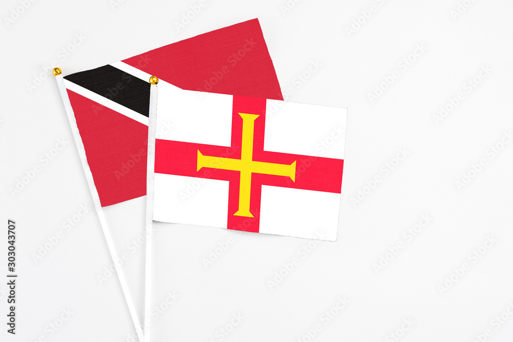 Guernsey and Trinidad And Tobago stick flags on white background. High quality fabric, miniature national flag. Peaceful global concept.White floor for copy space.