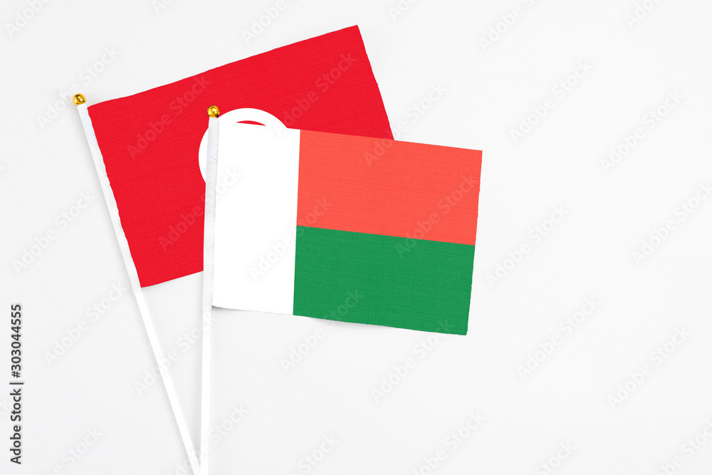 Fototapeta premium Madagascar and Tunisia stick flags on white background. High quality fabric, miniature national flag. Peaceful global concept.White floor for copy space.