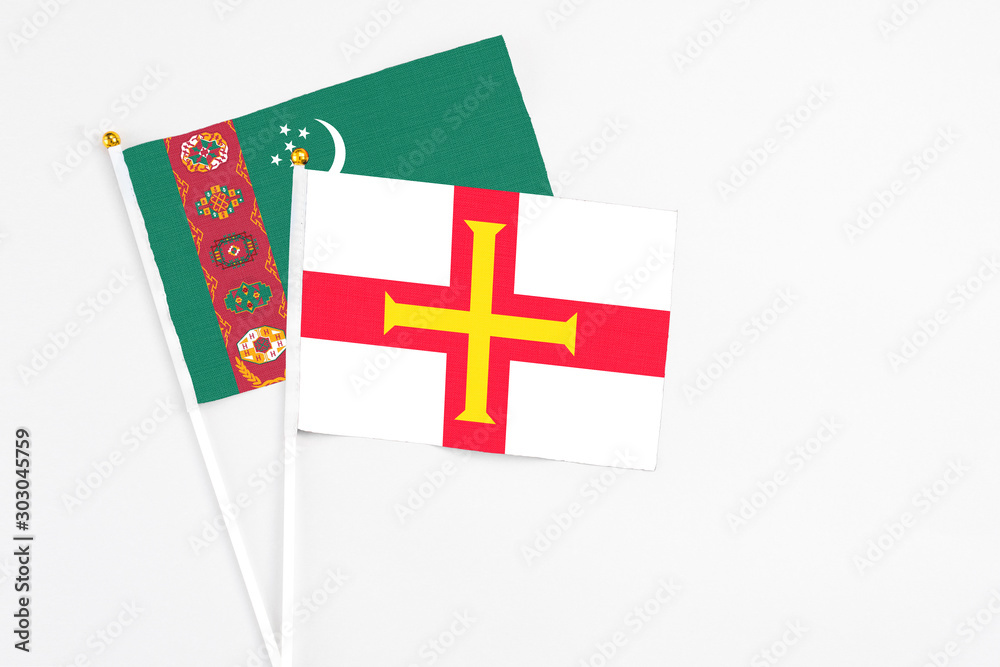 Guernsey and Turkmenistan stick flags on white background. High quality fabric, miniature national flag. Peaceful global concept.White floor for copy space.