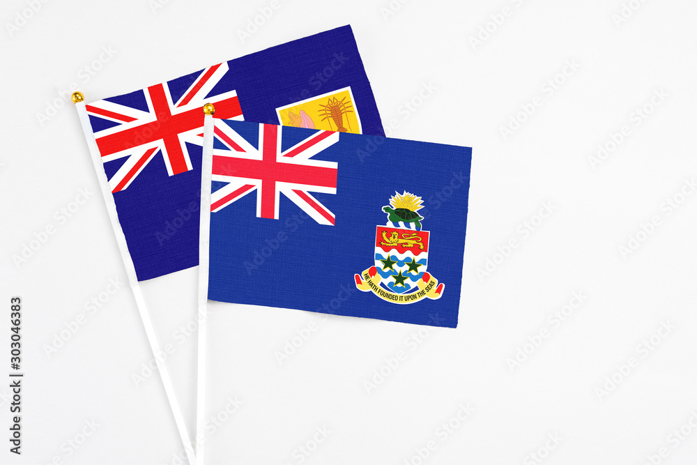 Fototapeta premium Cayman Islands and Turks And Caicos Islands stick flags on white background. High quality fabric, miniature national flag. Peaceful global concept.White floor for copy space.