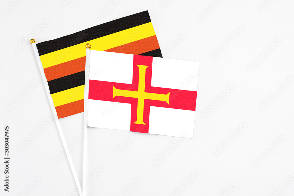 Guernsey and Uganda stick flags on white background. High quality fabric, miniature national flag. Peaceful global concept.White floor for copy space.