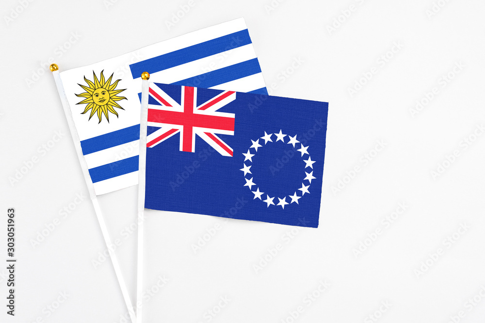Fototapeta premium Cook Islands and Uruguay stick flags on white background. High quality fabric, miniature national flag. Peaceful global concept.White floor for copy space.