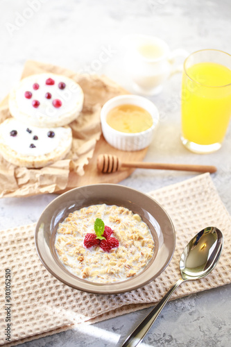 Baked granola with milk and raspberries in a plate, whole grain breads and freshly squeezed juice. A wholesome and dietary breakfast. Delicious muesli