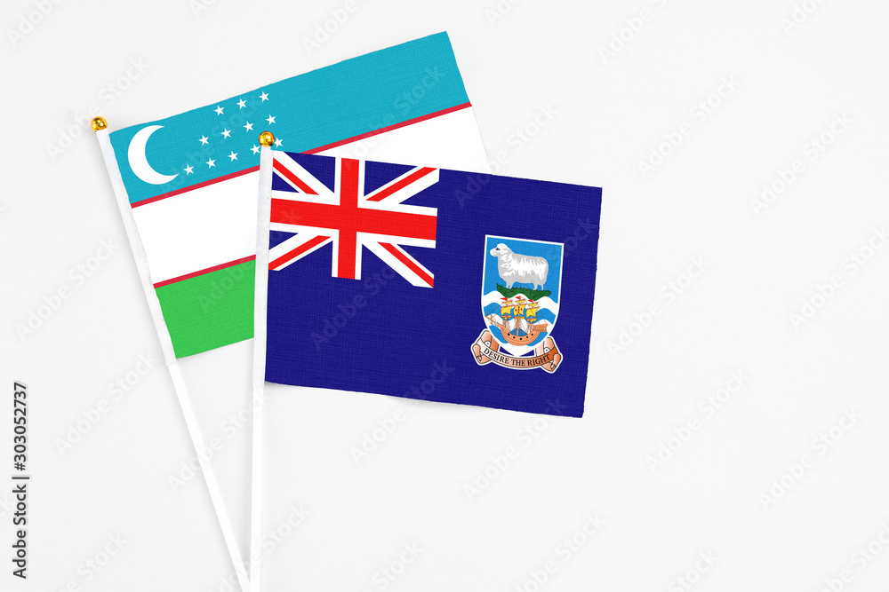 Fototapeta premium Falkland Islands and Uzbekistan stick flags on white background. High quality fabric, miniature national flag. Peaceful global concept.White floor for copy space.