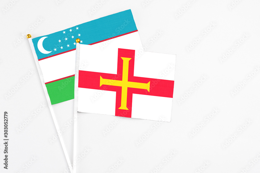 Guernsey and Uzbekistan stick flags on white background. High quality fabric, miniature national flag. Peaceful global concept.White floor for copy space.