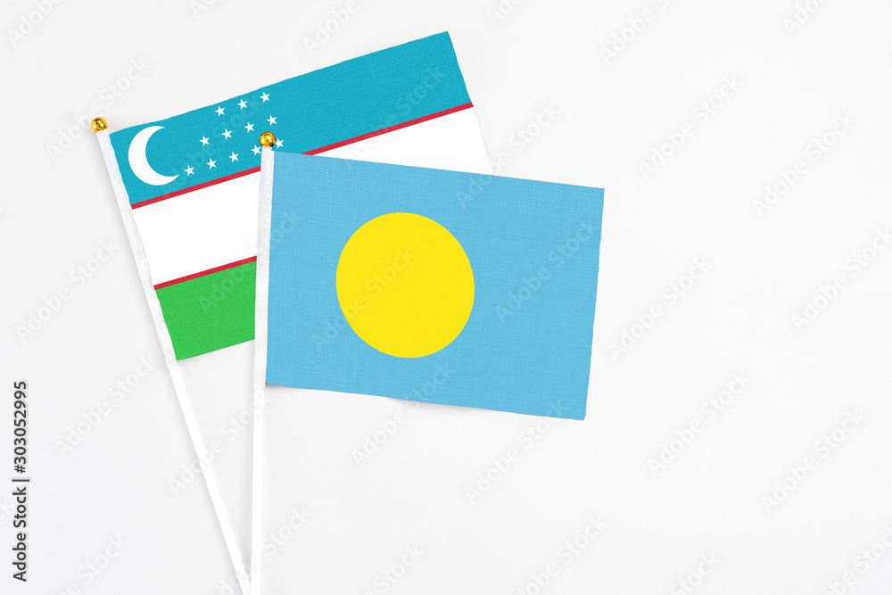 Palau and Uzbekistan stick flags on white background. High quality fabric, miniature national flag. Peaceful global concept.White floor for copy space.