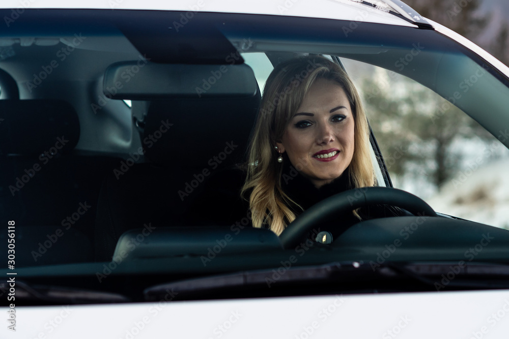 Blonde woman sits at a white car steering and seen through the window. Blonde woman sits at a white car steering and seen through the window.