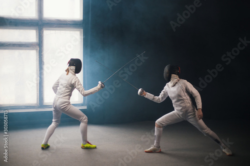A fencing training in the studio - two women in white protective costumes having a duel