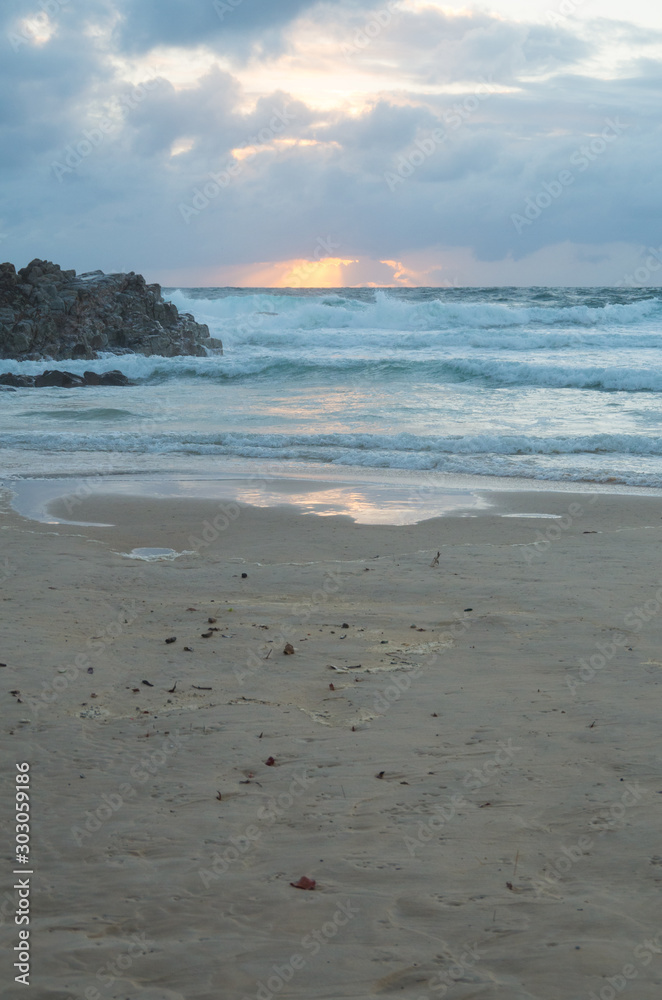 Sun rising over the horizon at a beach by a headland