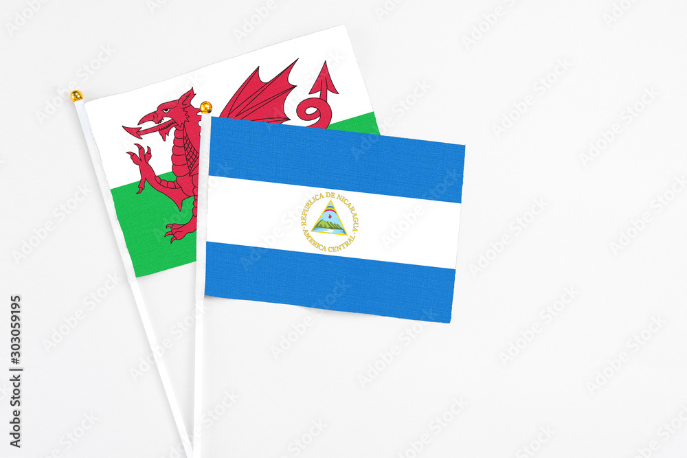 Nicaragua and Wales stick flags on white background. High quality fabric, miniature national flag. Peaceful global concept.White floor for copy space. Nicaragua and Wales stick flags on white background. High quality fabric, miniature national flag. Peaceful global concept.White floor for copy space.