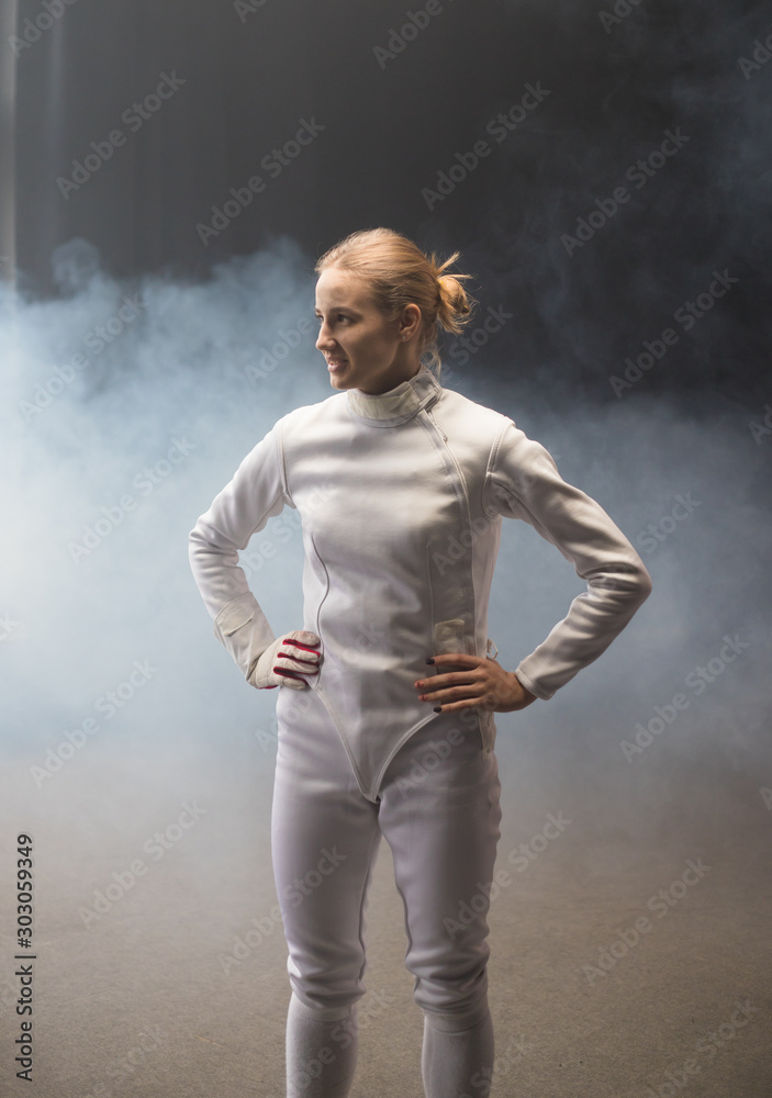 A young smiling woman fencer standing in the dark smoky studio