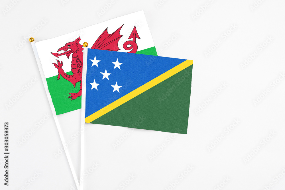 Solomon Islands and Wales stick flags on white background. High quality fabric, miniature national flag. Peaceful global concept.White floor for copy space. Solomon Islands and Wales stick flags on white background. High quality fabric, miniature national flag. Peaceful global concept.White floor for copy space.