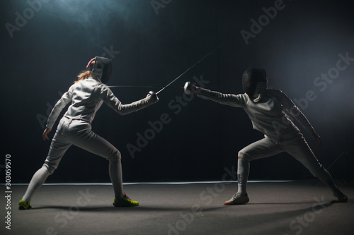 A fencing training in the studio - two women in protective suits having a duel