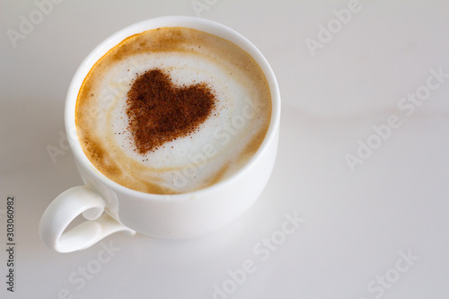 white cup with coffee and a patterned heart on milk foam