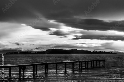 View of a pier on a lake, with a ray of sun against a moody sky
