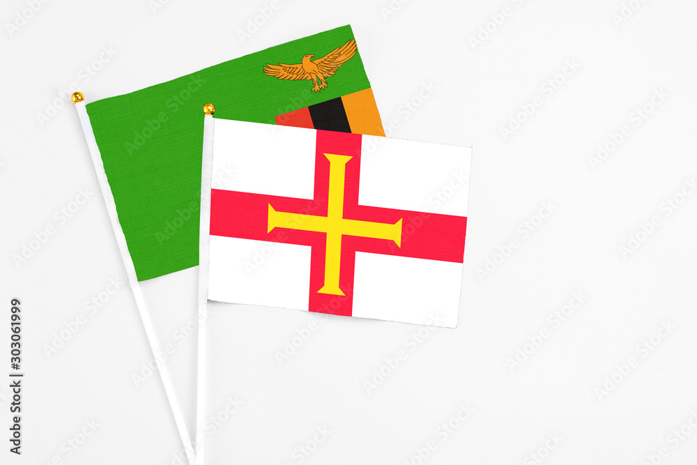 Guernsey and Zambia stick flags on white background. High quality fabric, miniature national flag. Peaceful global concept.White floor for copy space.