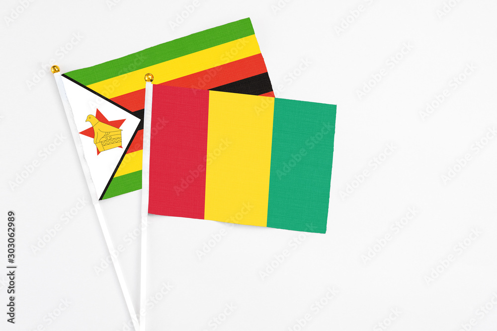 Guinea and Zimbabwe stick flags on white background. High quality fabric, miniature national flag. Peaceful global concept.White floor for copy space.
