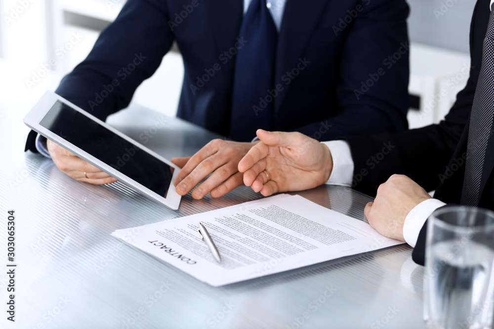 Business people using tablet computer while working together at the desk in modern office. Unknown businessman or male entrepreneur with colleague at workplace. Teamwork and partnership concept Business people using tablet computer while working together at the desk in modern office. Unknown businessman or male entrepreneur with colleague at workplace. Teamwork and partnership concept