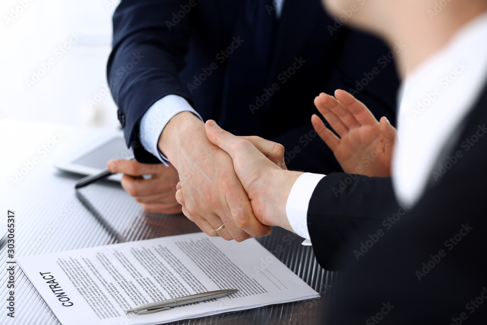 Obraz premium Business people shaking hands after contract signing at the glass desk in modern office. Unknown businessman, male entrepreneur with colleagues at meeting or negotiation. Teamwork, partnership and
