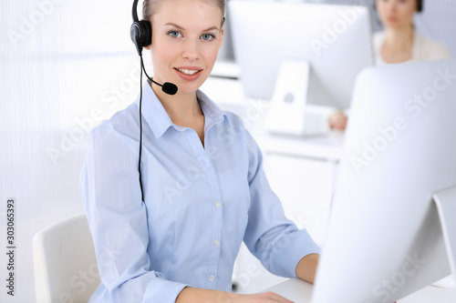 Call center office. Beautiful blonde woman using computer and headset for consulting clients online. Group of operators working as customer service occupation. Business people concept photo