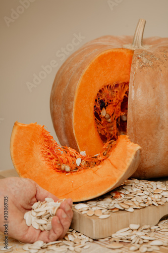 Ripe sliced ​​pumpkin lies on board. Nearby hand hold seeds