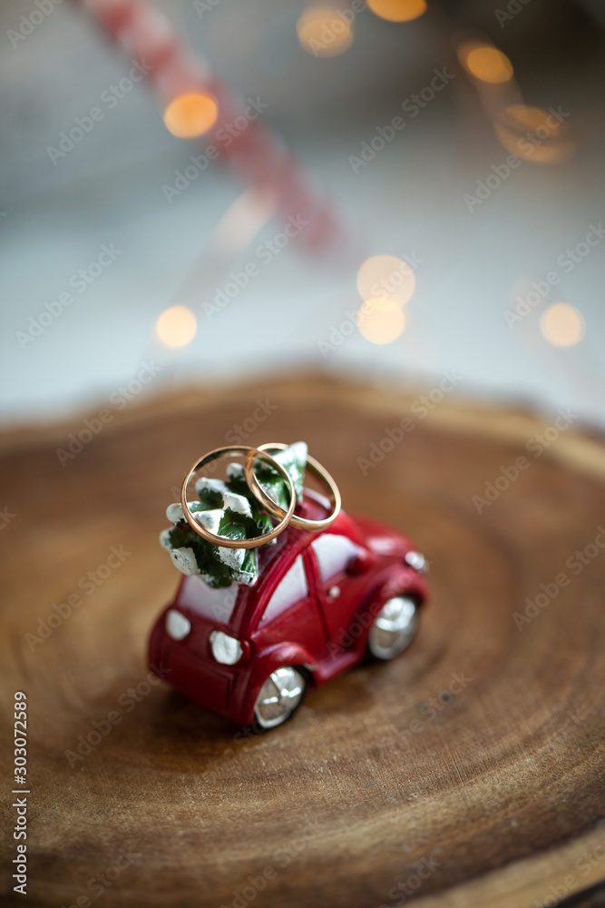 Fototapeta premium Red toy car with a christmas tree on the roof and two wedding ring, with bokeh on background. new year wedding concept