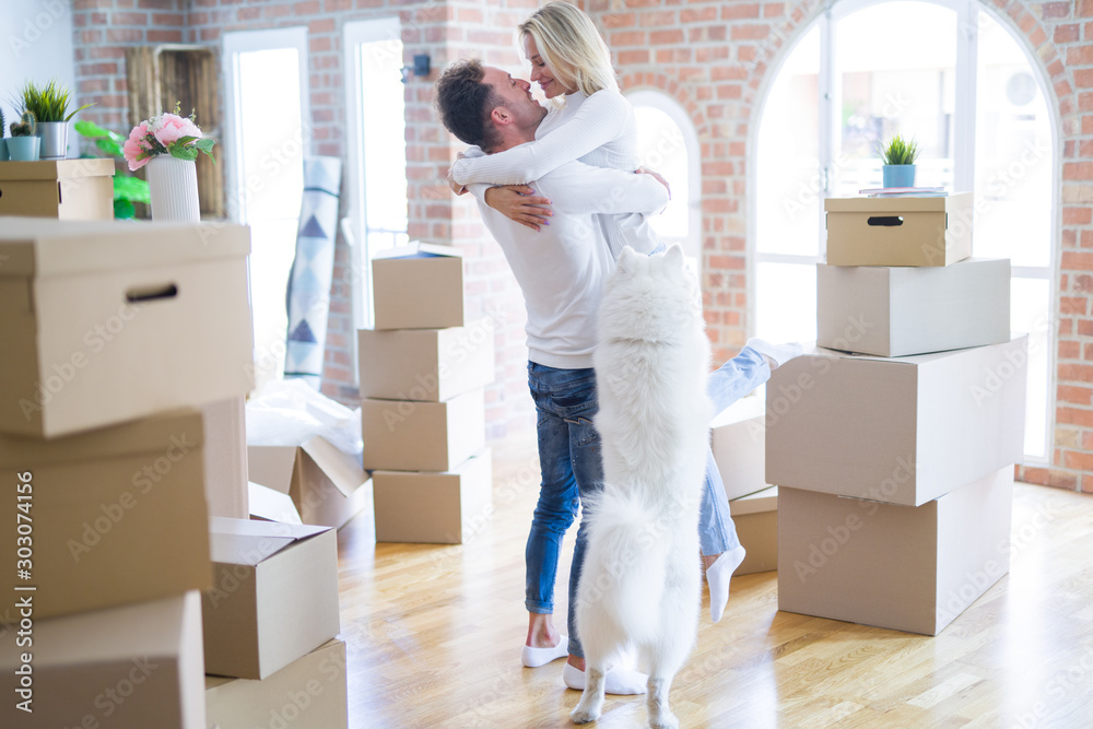 Young beautiful couple with dog hugging at new home around cardboard boxes Young beautiful couple with dog hugging at new home around cardboard boxes