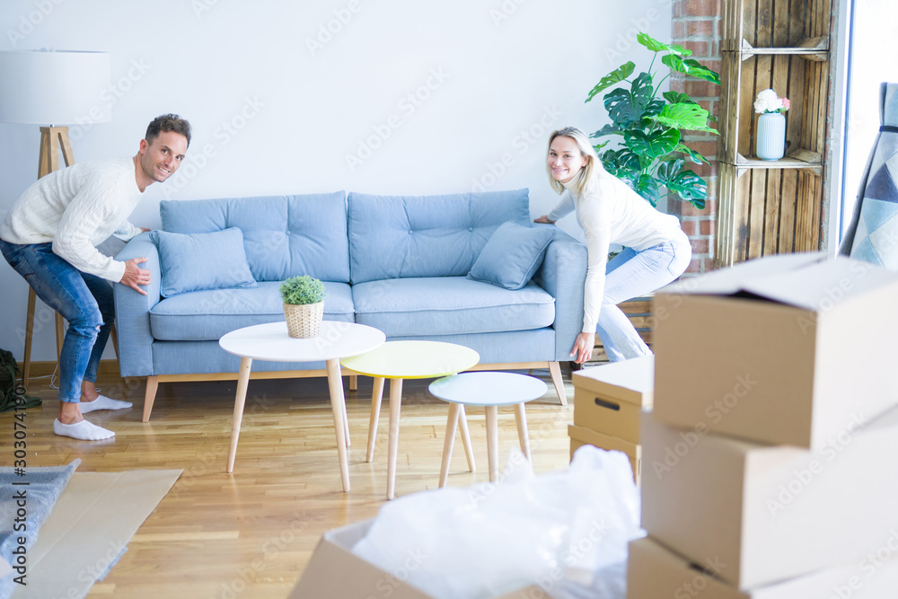 Young beautiful couple moving sofa at new home around cardboard boxes Young beautiful couple moving sofa at new home around cardboard boxes