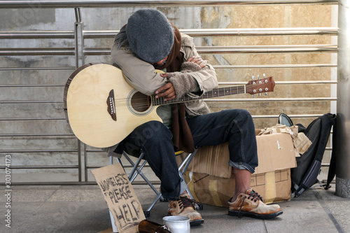 a old man is homeless or beggar sitting or sleeping beside street with cup for request some coin from kindness man and text please help