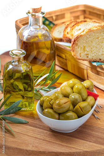 Artisan olives (canned in extra virgin olive oil, vinegar, spices) with red peppers and garlic. Includes olive tree leaves and bottle of extra virgin olive oil. Wooden board background.