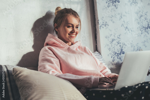 Tableau sur toile Young cheerful woman sit on sofa and type on laptop