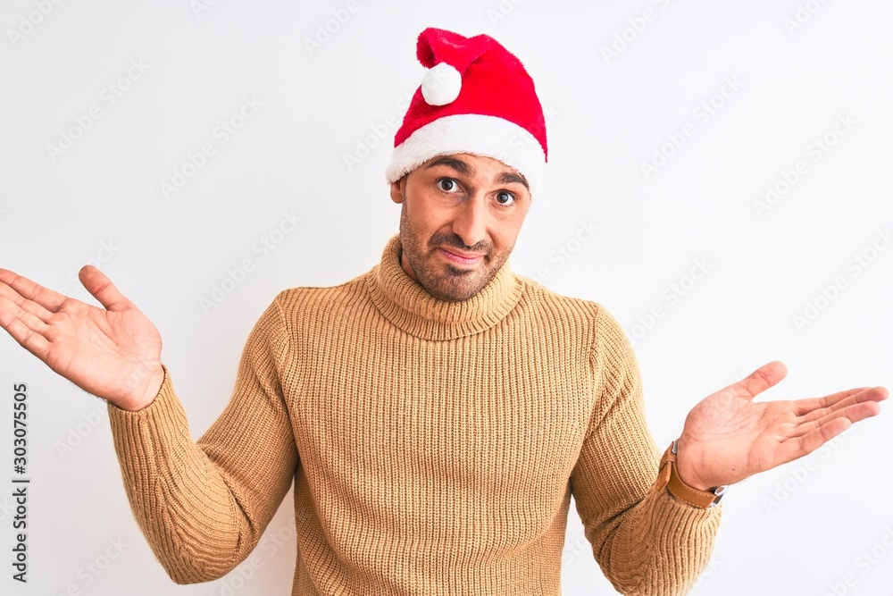 Naklejka premium Young handsome man wearing christmas and turtleneck sweater over isolated background clueless and confused expression with arms and hands raised. Doubt concept.