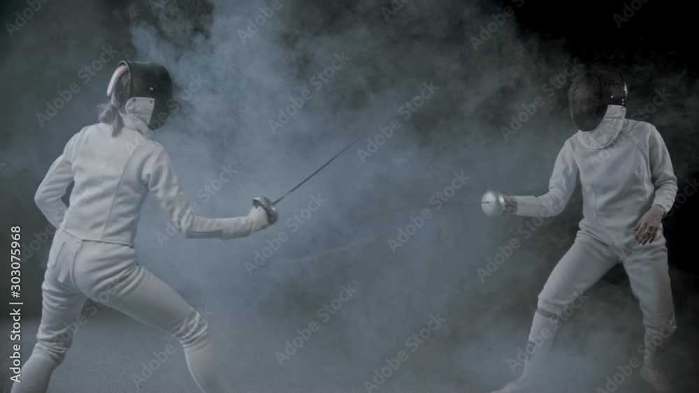 Fencing training - two women having a duel in the smoky studio Fencing training - two women having a duel in the smoky studio