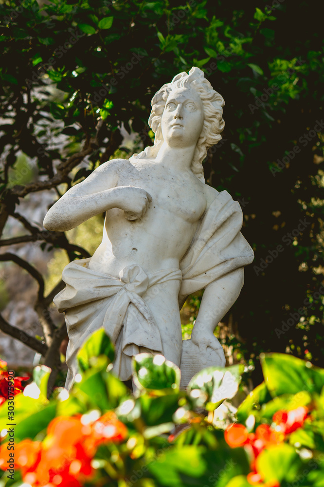 beautiful statue in a garden with red flowers in the foreground