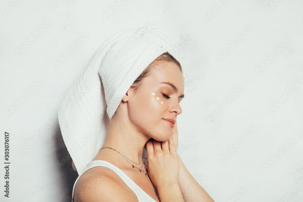 Attractive nice young woman with natural beauty posing. Side view. Model hold hands close to cheek. White towel around hair. Morning or evening beauty routine after bath. Isolated on grey background. Attractive nice young woman with natural beauty posing. Side view. Model hold hands close to cheek. White towel around hair. Morning or evening beauty routine after bath. Isolated on grey background.