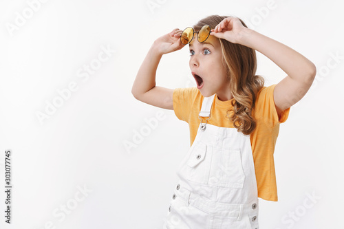 Wondered impressed little gorgeous girl, child travel abroad parents look fascinated turn left ambushed, take-off glasses speechless and astonished, seeing awesome offer, white background